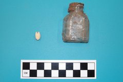 Bead and medicine bottle artifacts on a blue background next a ruler for size