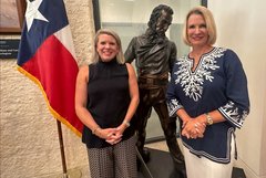 Dr. Kate Rogers and Dr. Dawn Buckingham in front of a bronze statue and Texas State flag