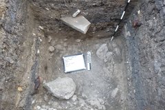 Inside a square excavation unit with a marker and a small whiteboard at the bottom