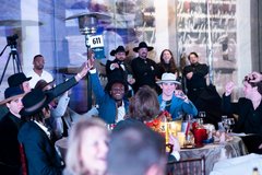 Young man holding up an auction bid paddle that says 611 as table guests cheer him on