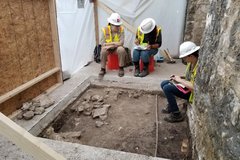 Three archaeologists making notes around an excavation site