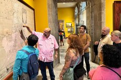 Curator in pink guayabera shirt pointing at map with a group of educators watching