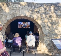 Guests seated on benches watching a film in the Alamo Long Barrack