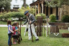 Three children lined up learning how to fire a musket with an Alamo Living Historian