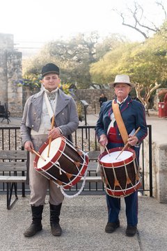 Two male living historians in 1830s attire, each holding a drum