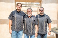 Three men in black guayabera shirts standing in front of a concrete gate