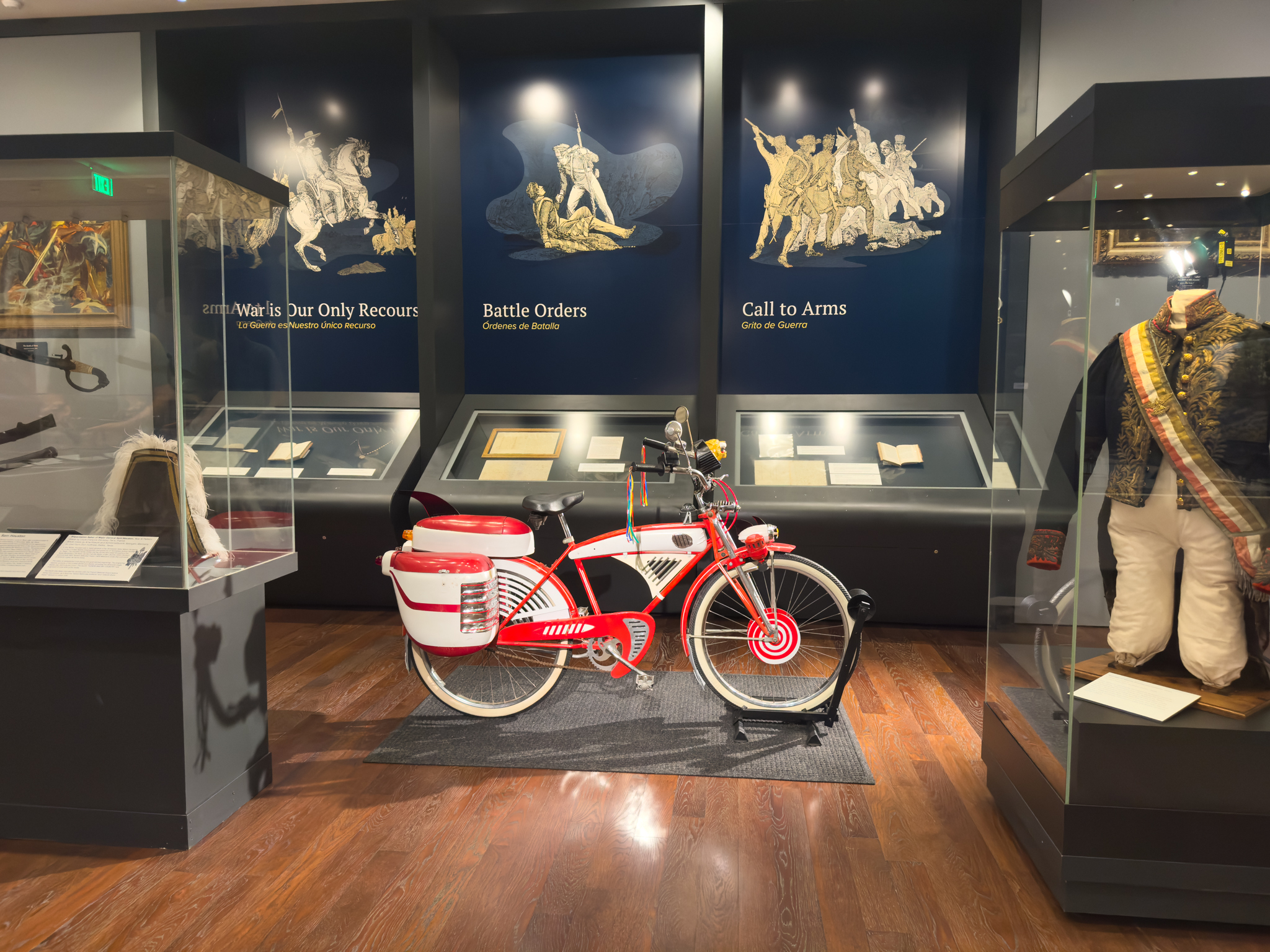 Red bicycle with white trim on the floor in front of exhibit cases