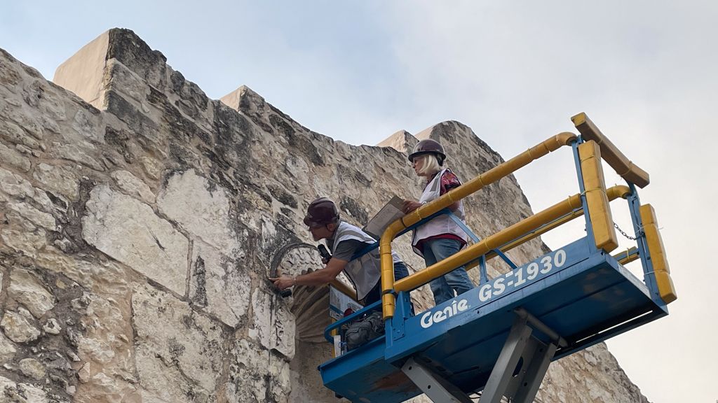 Women on a scissor lift examining stone on Alamo Church