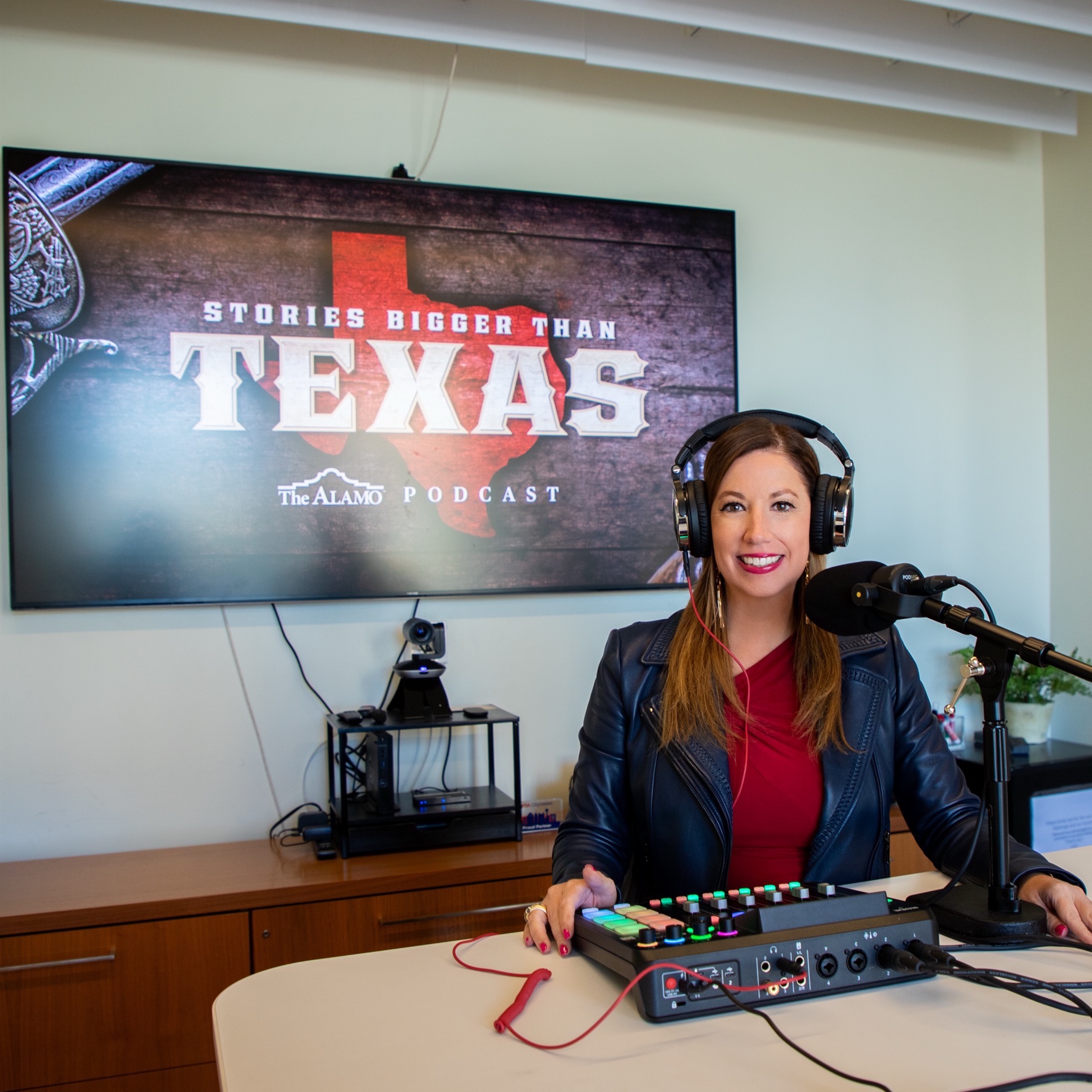 Woman wearing headphones smiling at the camera seated with podcast equipment on the table