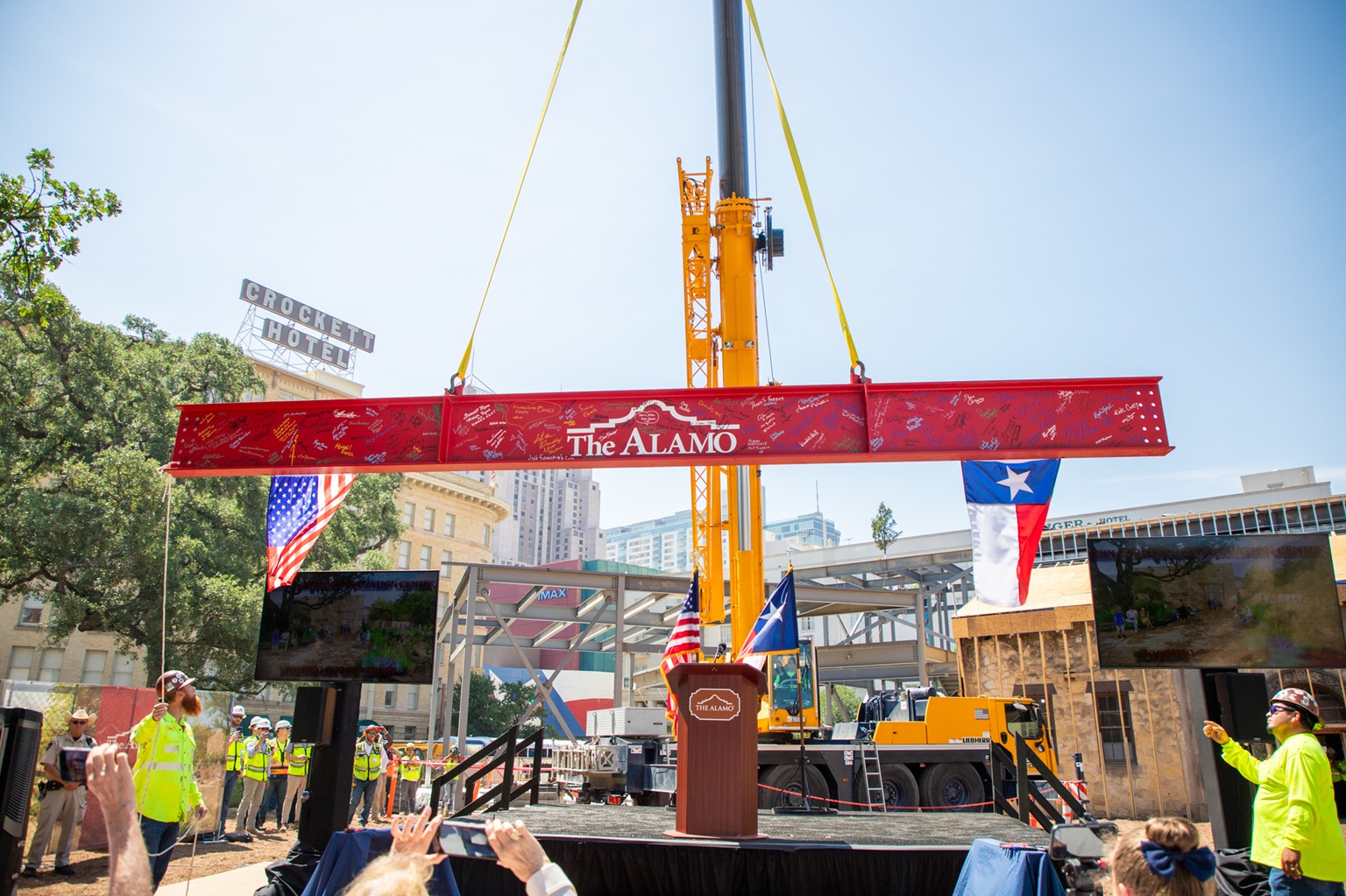 Crane lifting red metal beam with Alamo logo
