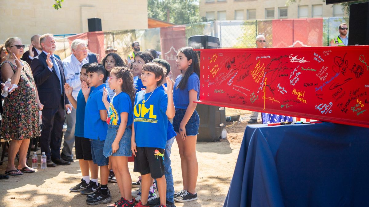 Children in blue shirts next to the red beam at an outdoor ceremony