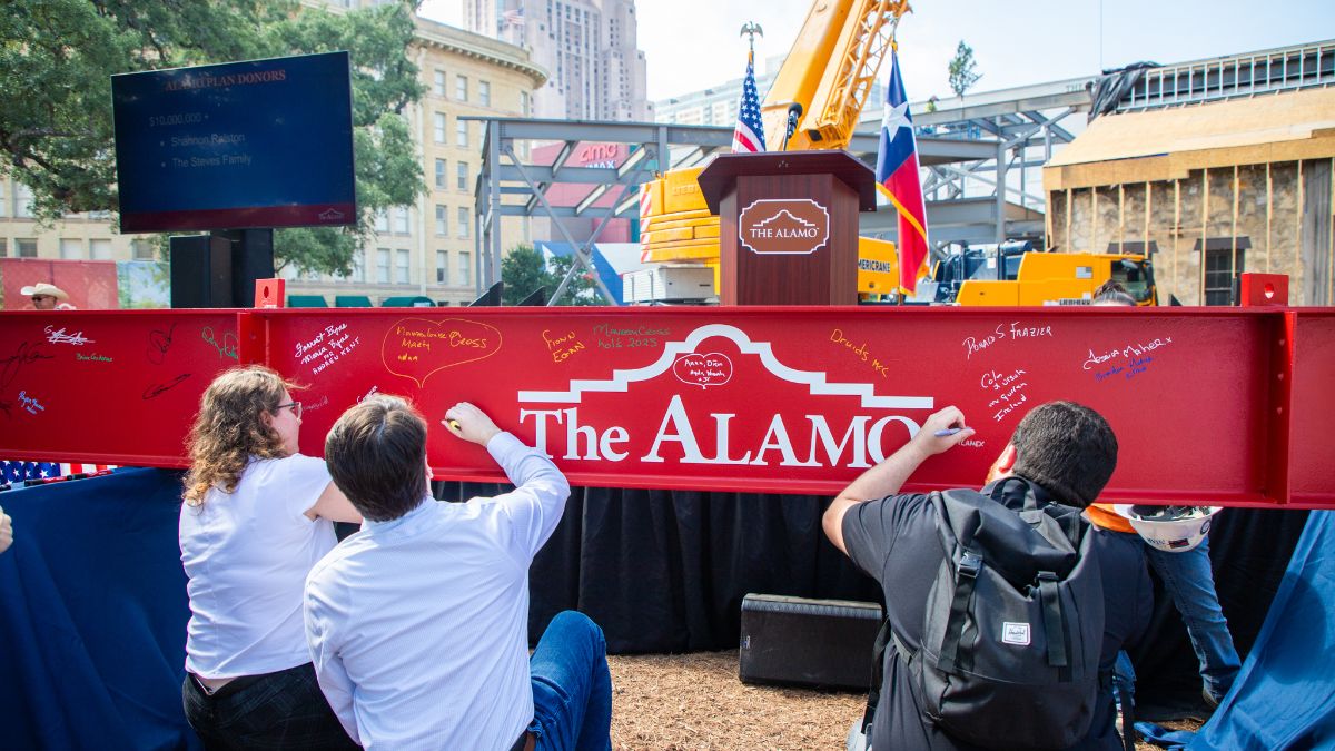 Guests signing a red metal beam with the Alamo logo at an outdoor event