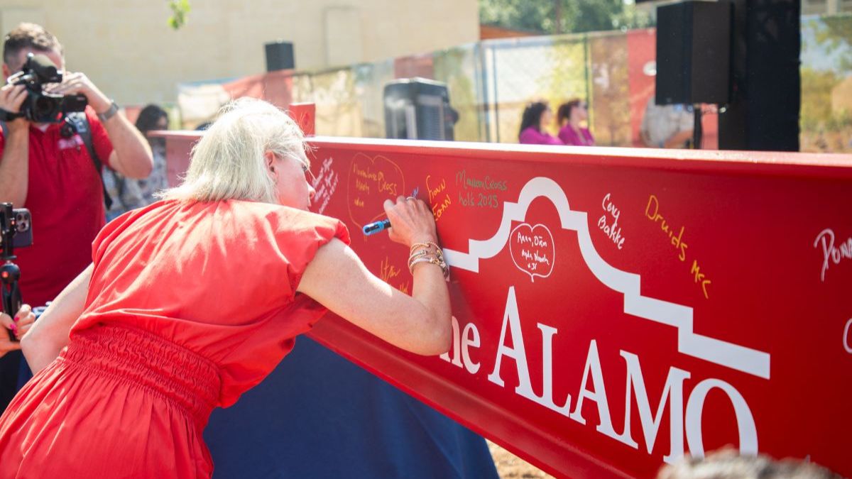 Dr. Kate Rogers signing a red metal beam with the Alamo logo