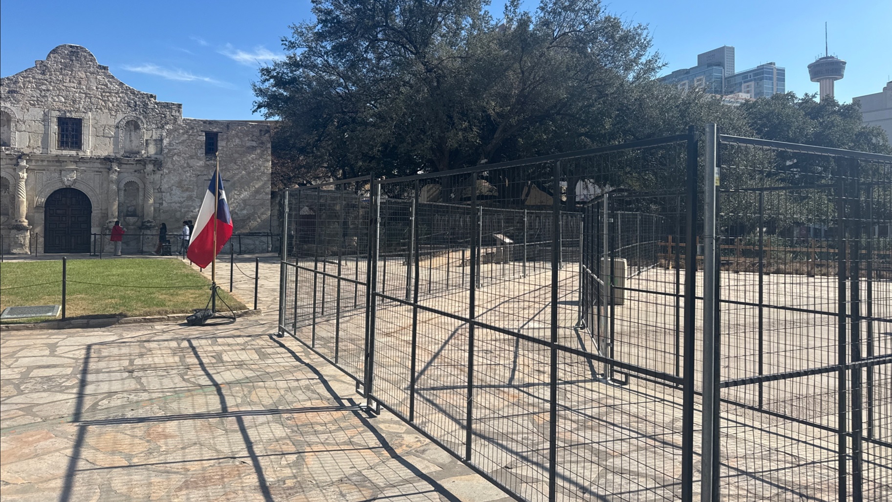 Fencing on limestone tile in front of Alamo Church green grass and Texas flag
