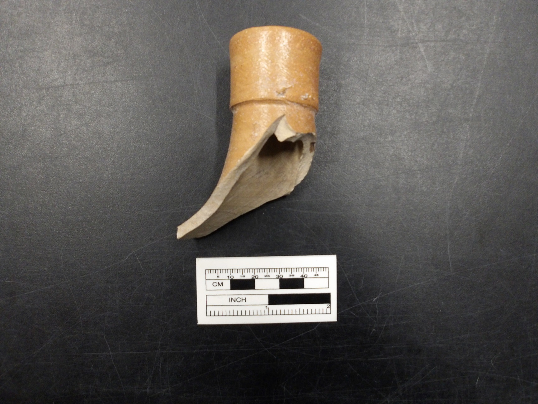 Broken piece of stoneware next to a ruler for size