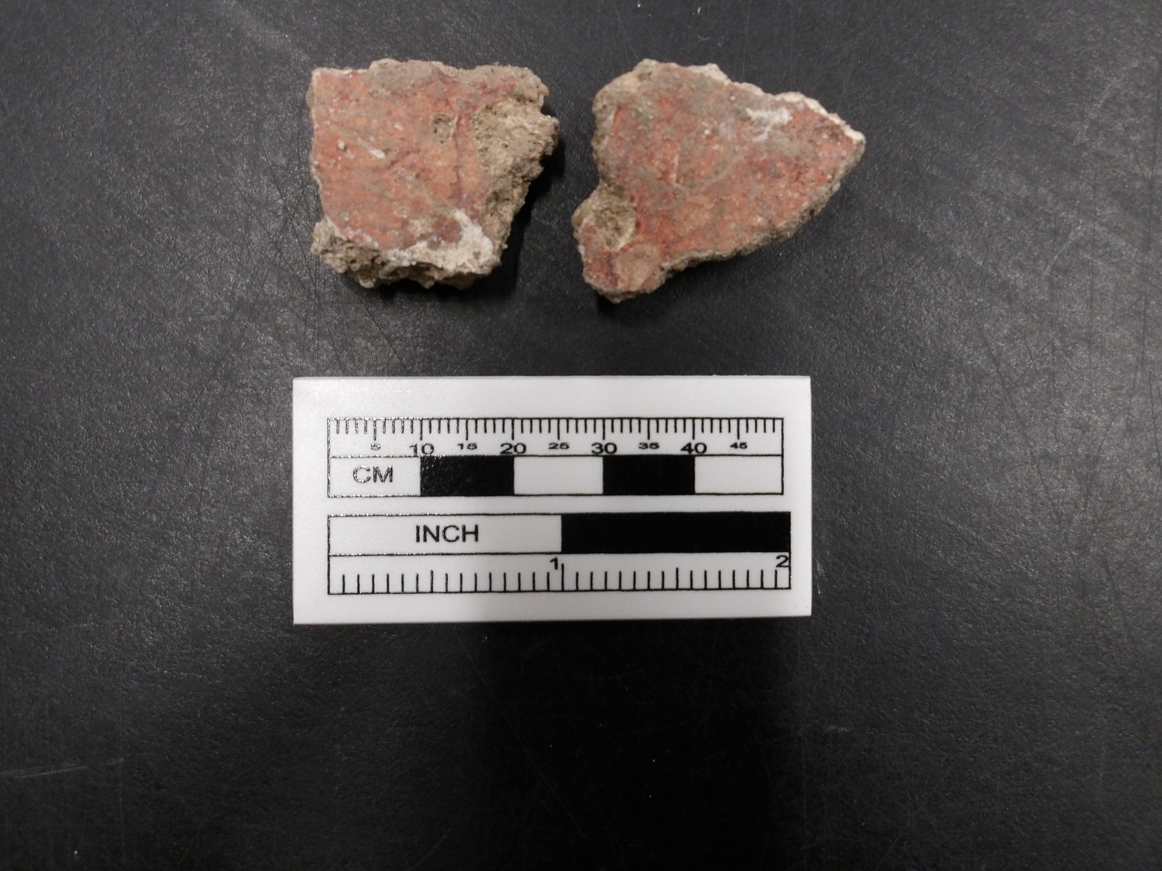 Two pieces of red painted plaster next to a ruler for size