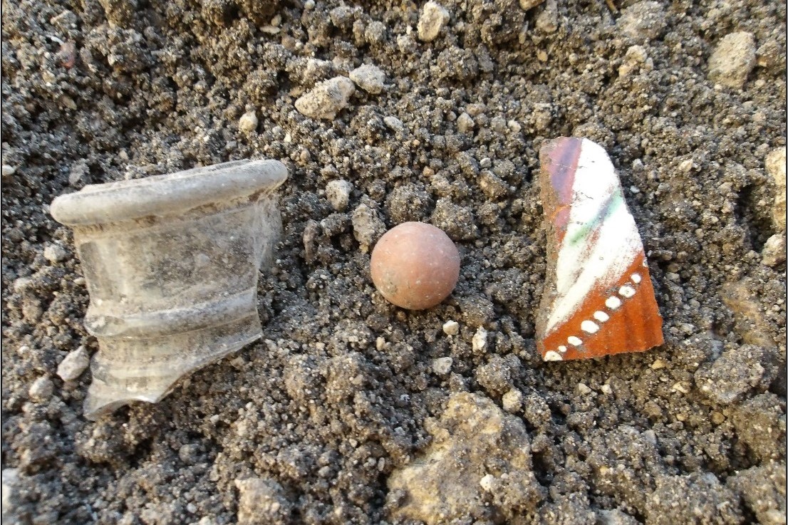 Glass bottle neck, clay marble, and Galera sherd on a bed of pebbles