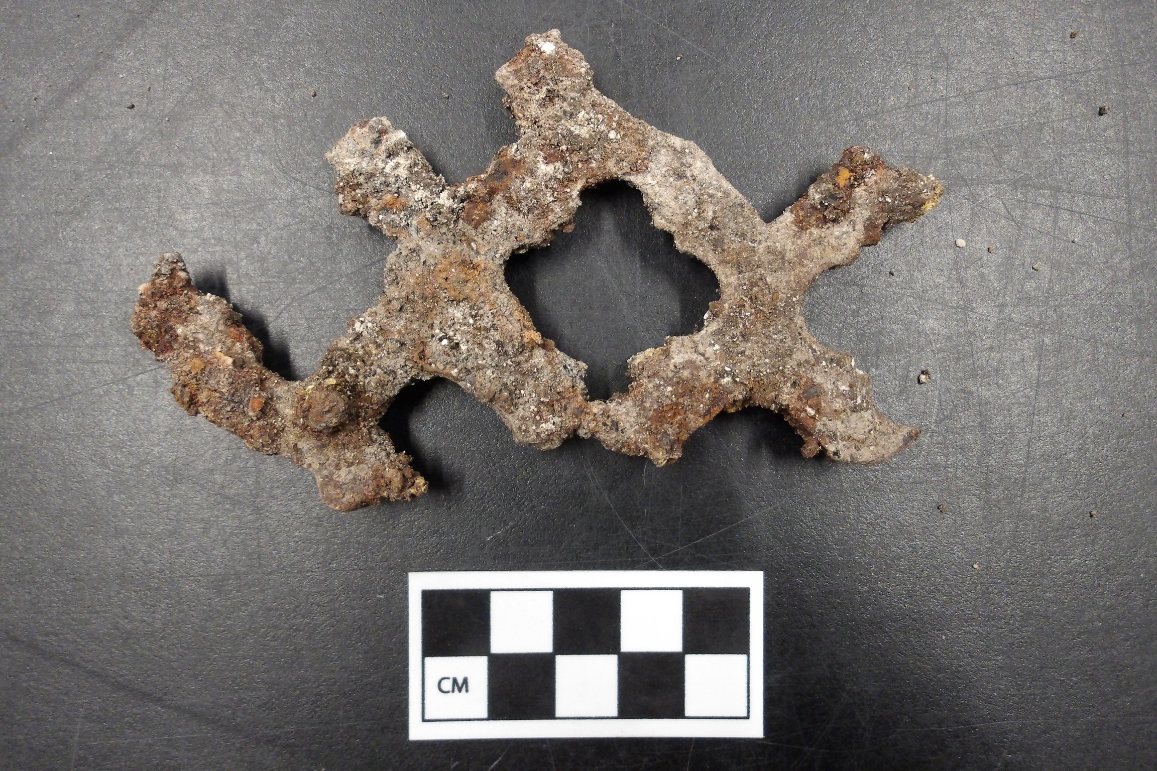 Metal hardware in an x pattern next to a ruler for size