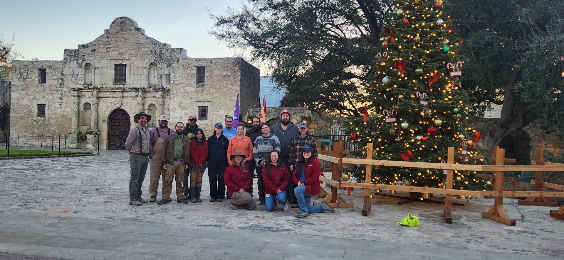 Group of archaeologists standing between Alamo Church and the Christmas tree in the plaza