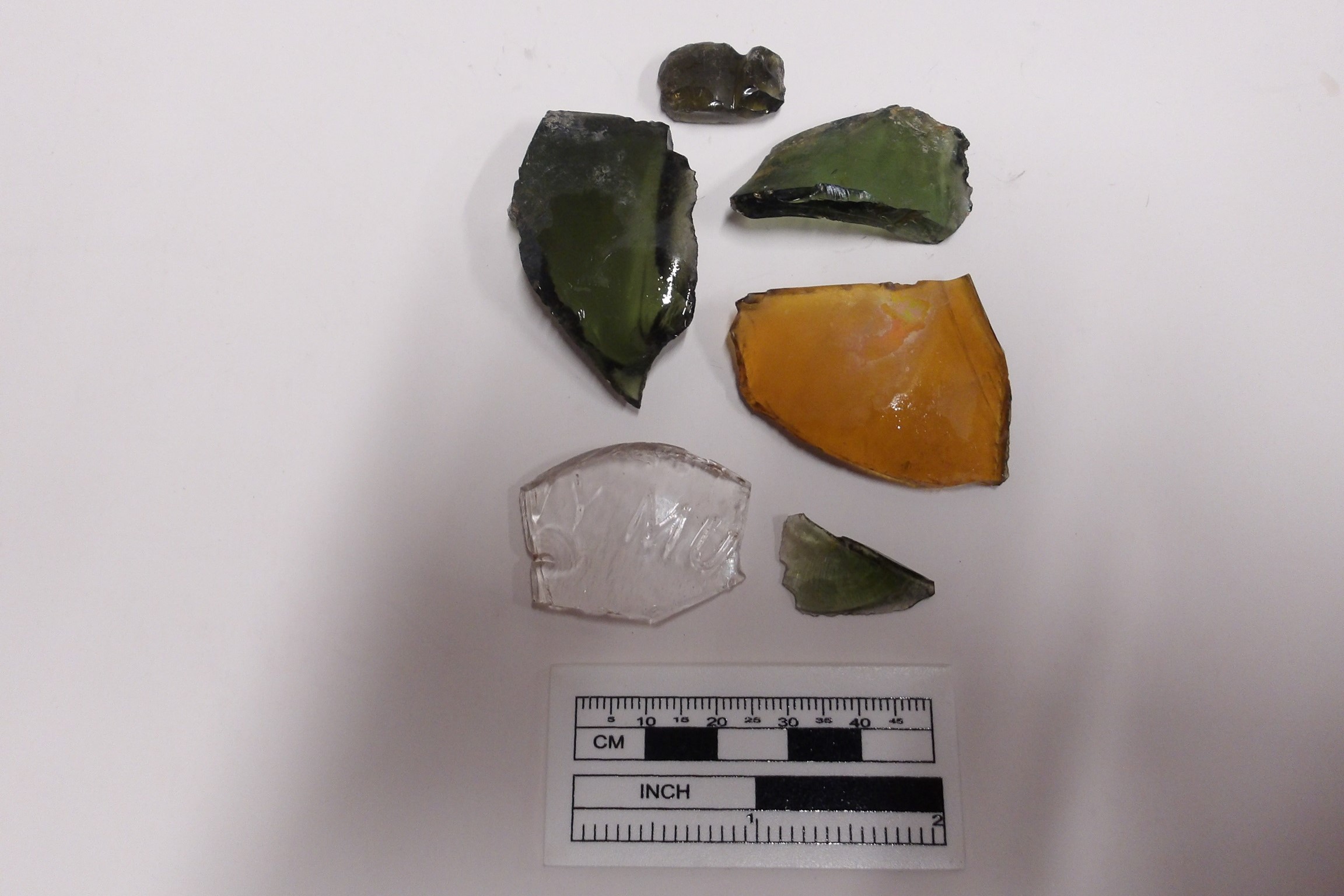 Six glass fragments on a white background next to a ruler for size