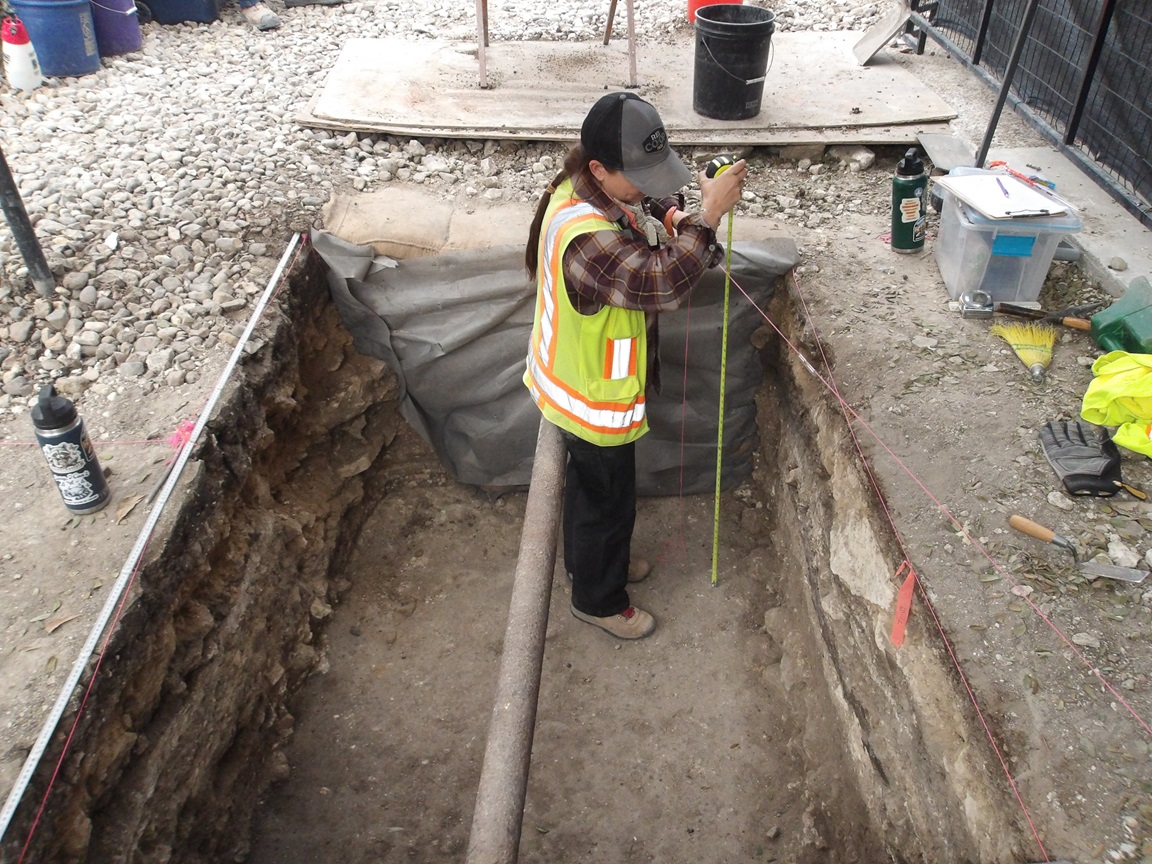 Archaeologist standing inside an excavation unit taking measurements