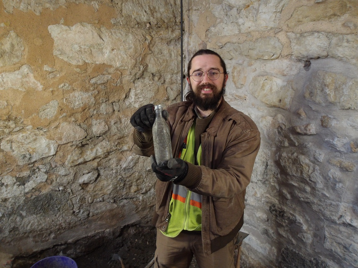 Archaeologist holding a glass bottle next to limestone walls