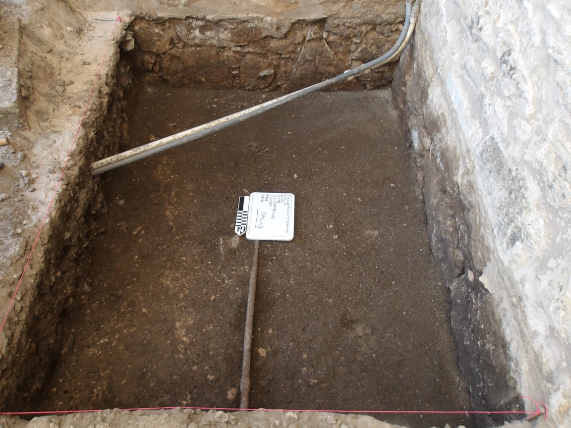 Dirt interior of excavation unit with a curved pipe across the top