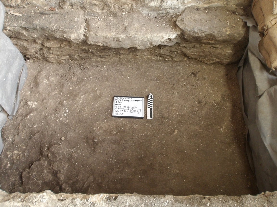Bottom of excavation unit with limestone edges and a whiteboard and ruler at the center bottom