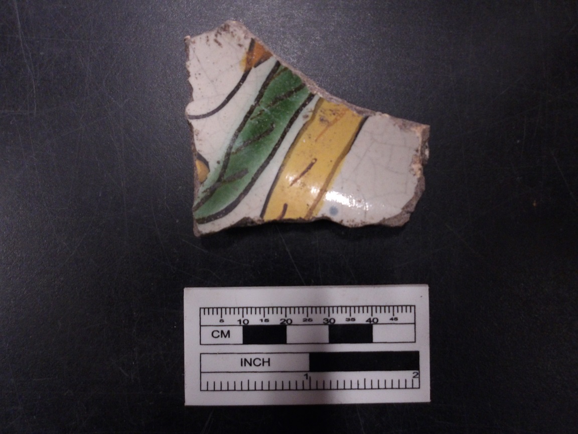 Ceramic sherd with green and yellow next to a ruler for size