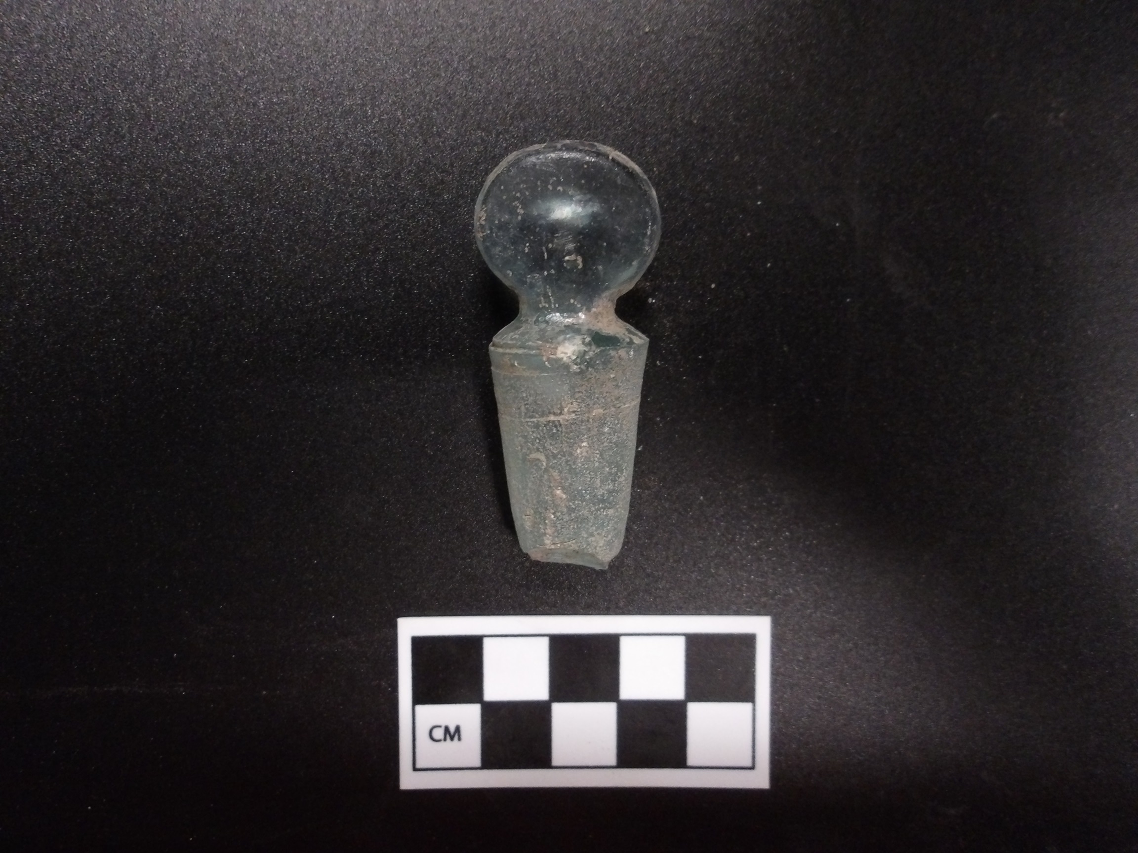 Glass bottle stopper on a black background next to a ruler for size