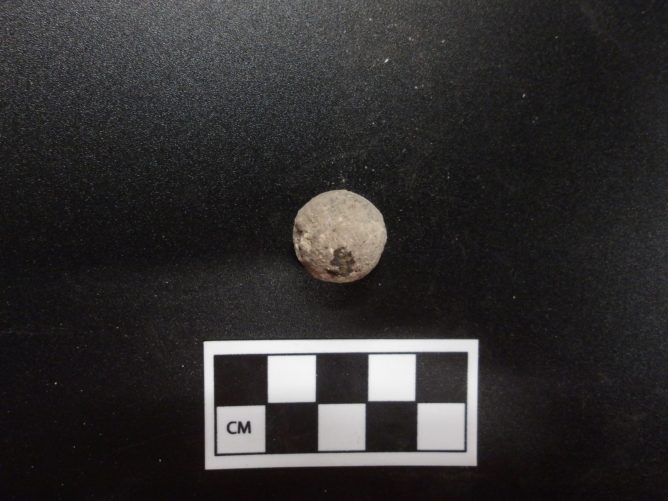 Musket ball on a black background next to a ruler for size