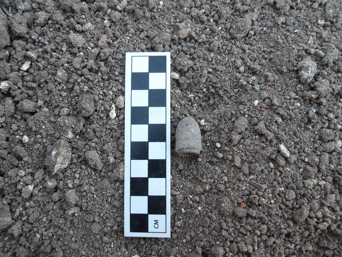 Minié ball on a bed of rocks next to a ruler for size