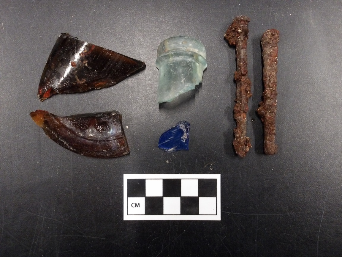 Glass artifacts and rusty nails next to a ruler for size