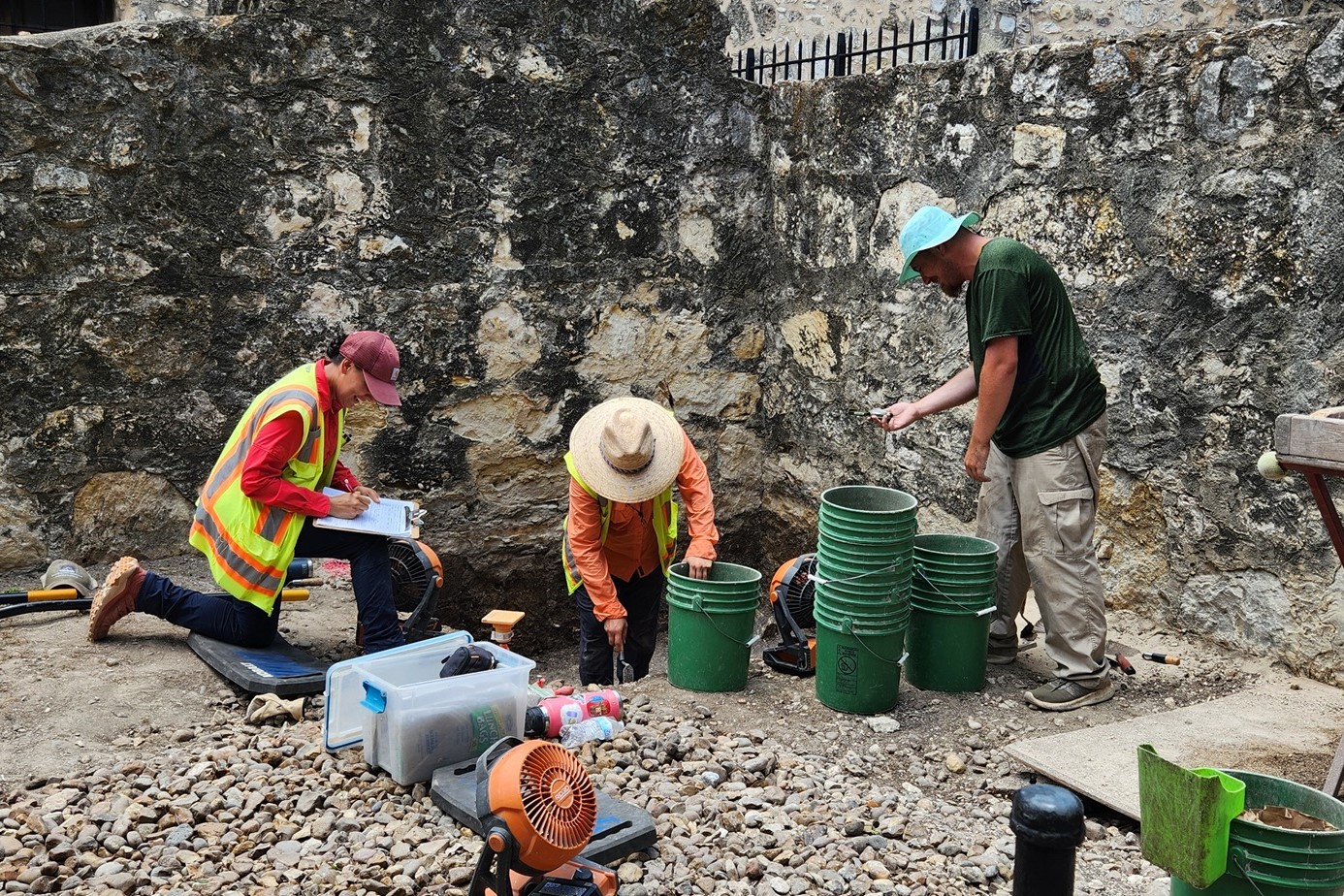 Three archaeologist working around an excavation unit outside of Alamo Church