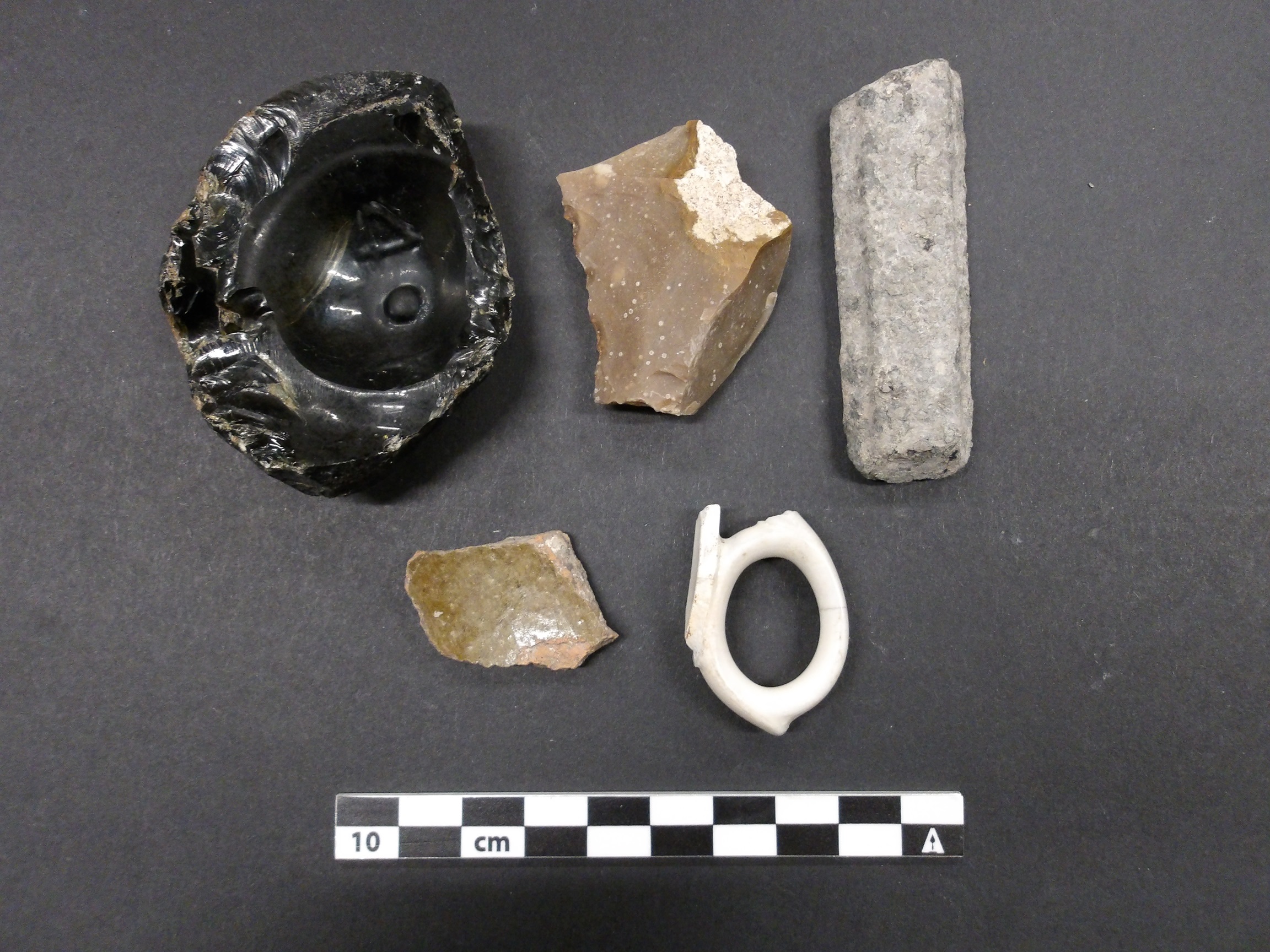 Ceramics, base of a dark olive glass container, and a biface artifacts from an excavation unit