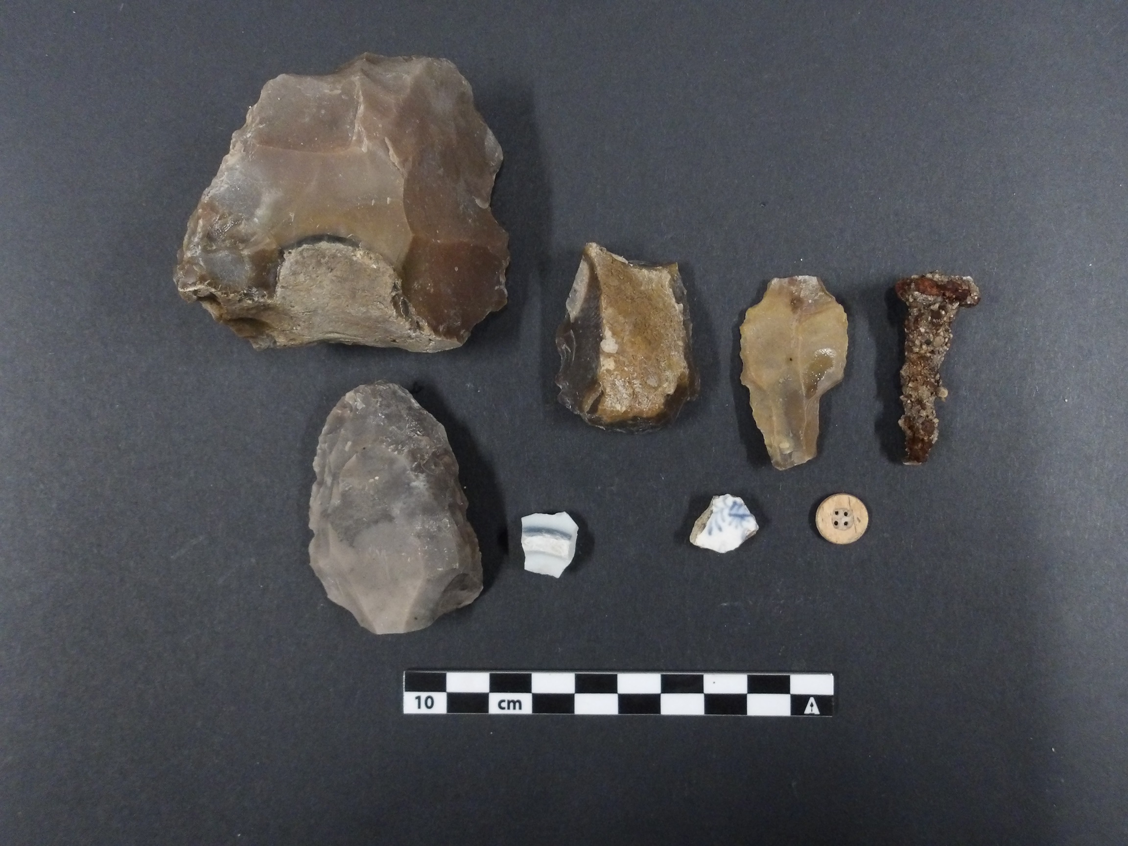 Artifacts from an excavation unit including rocks, ceramic fragments, and a button