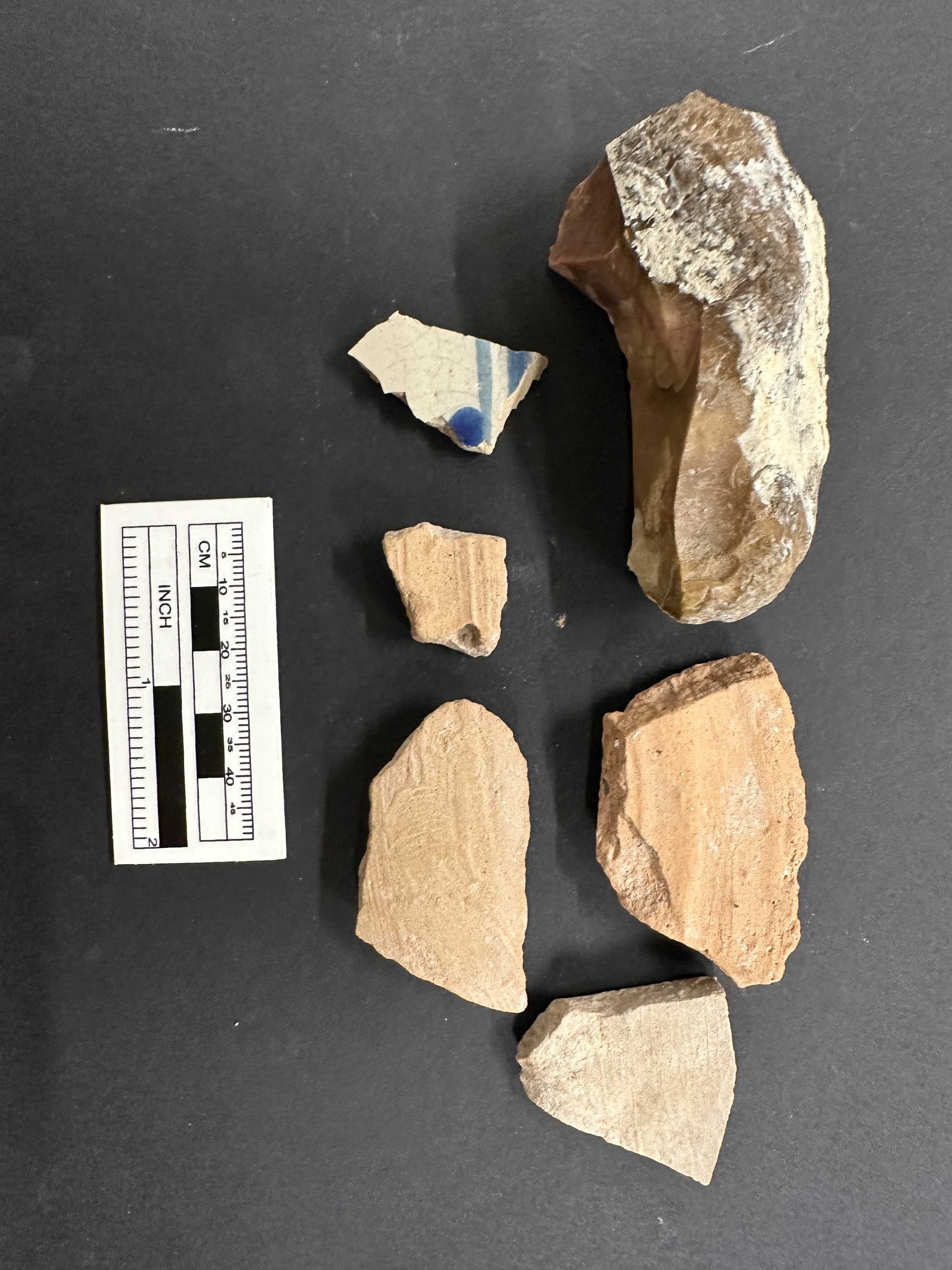 Ceramic and stone artifacts from an excavation unit next to a ruler for size