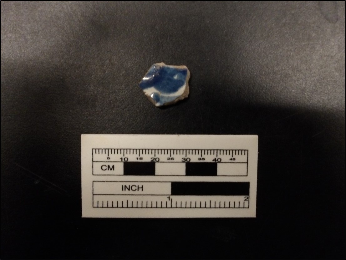 White ceramic sherd with puebla blue on a black background next to a ruler for size