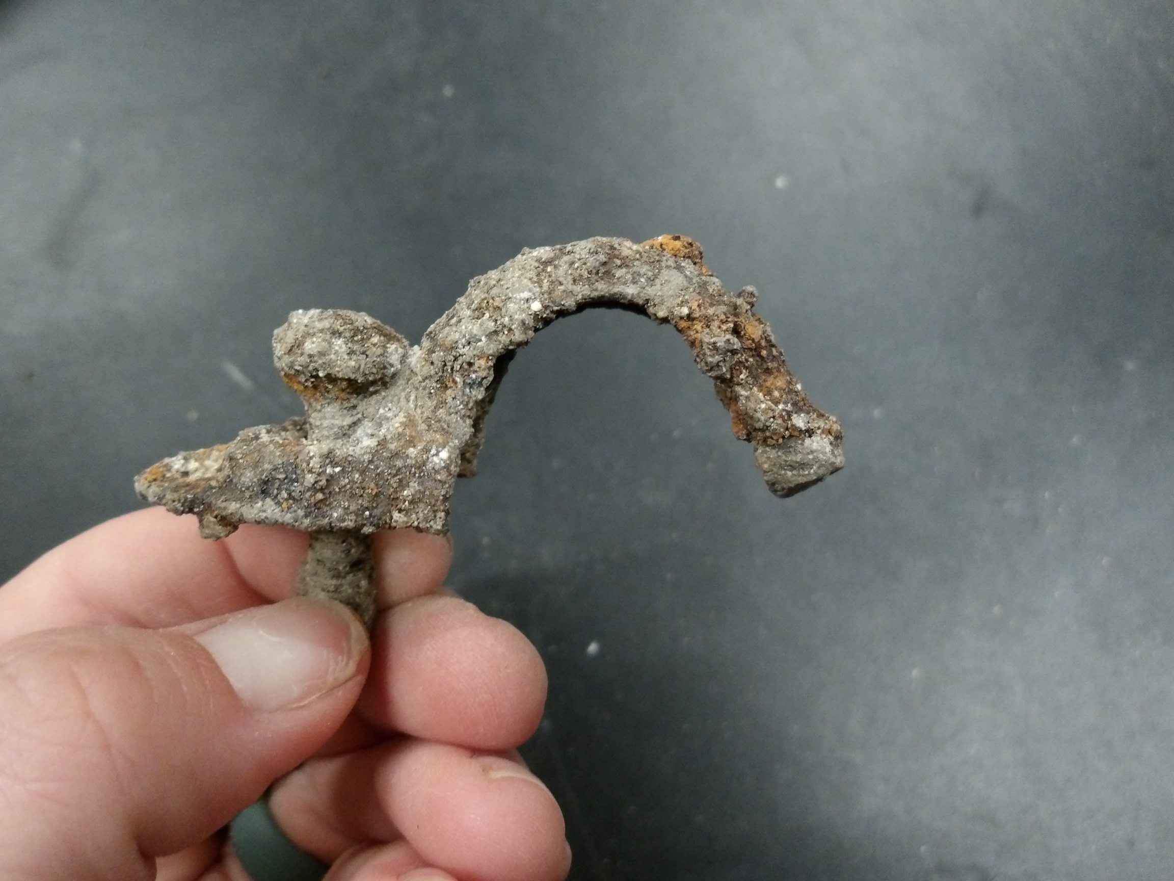 Hand holding a piece of metal hardware recovered from an excavation unit