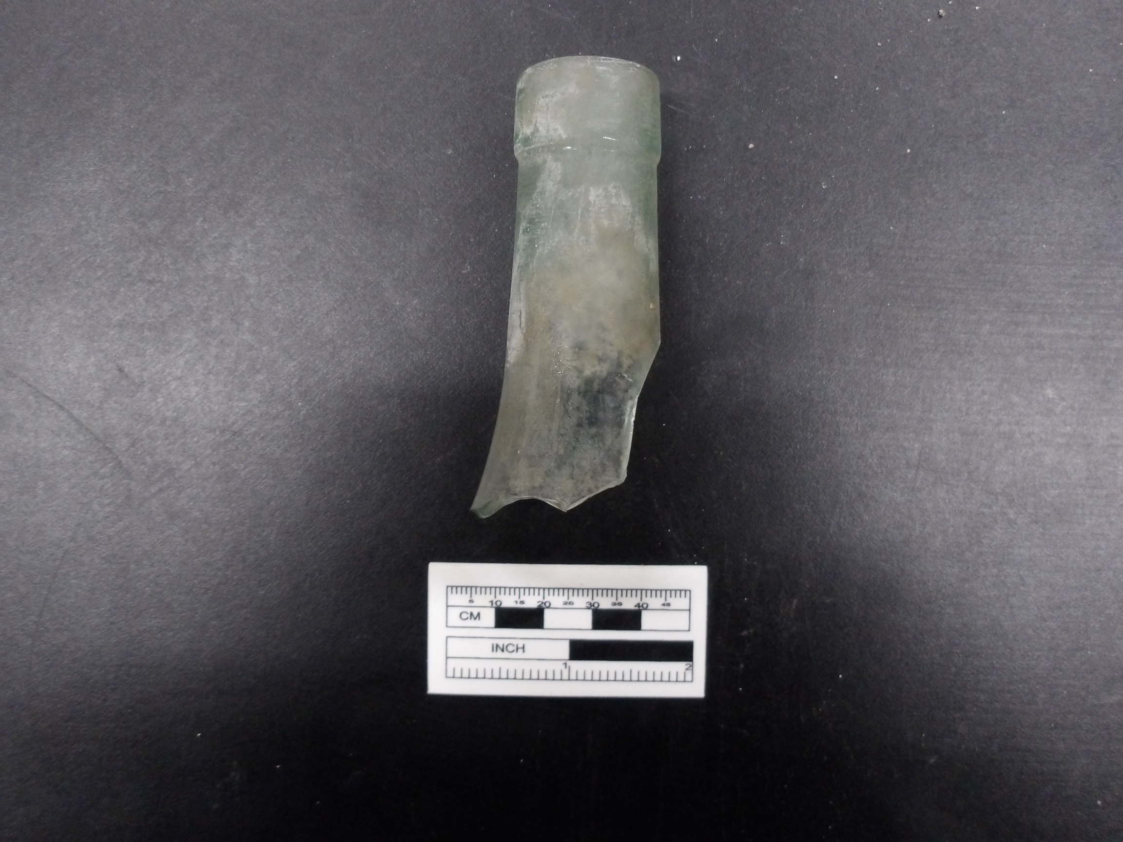 Top of a glass bottle on a black background next to a ruler for size