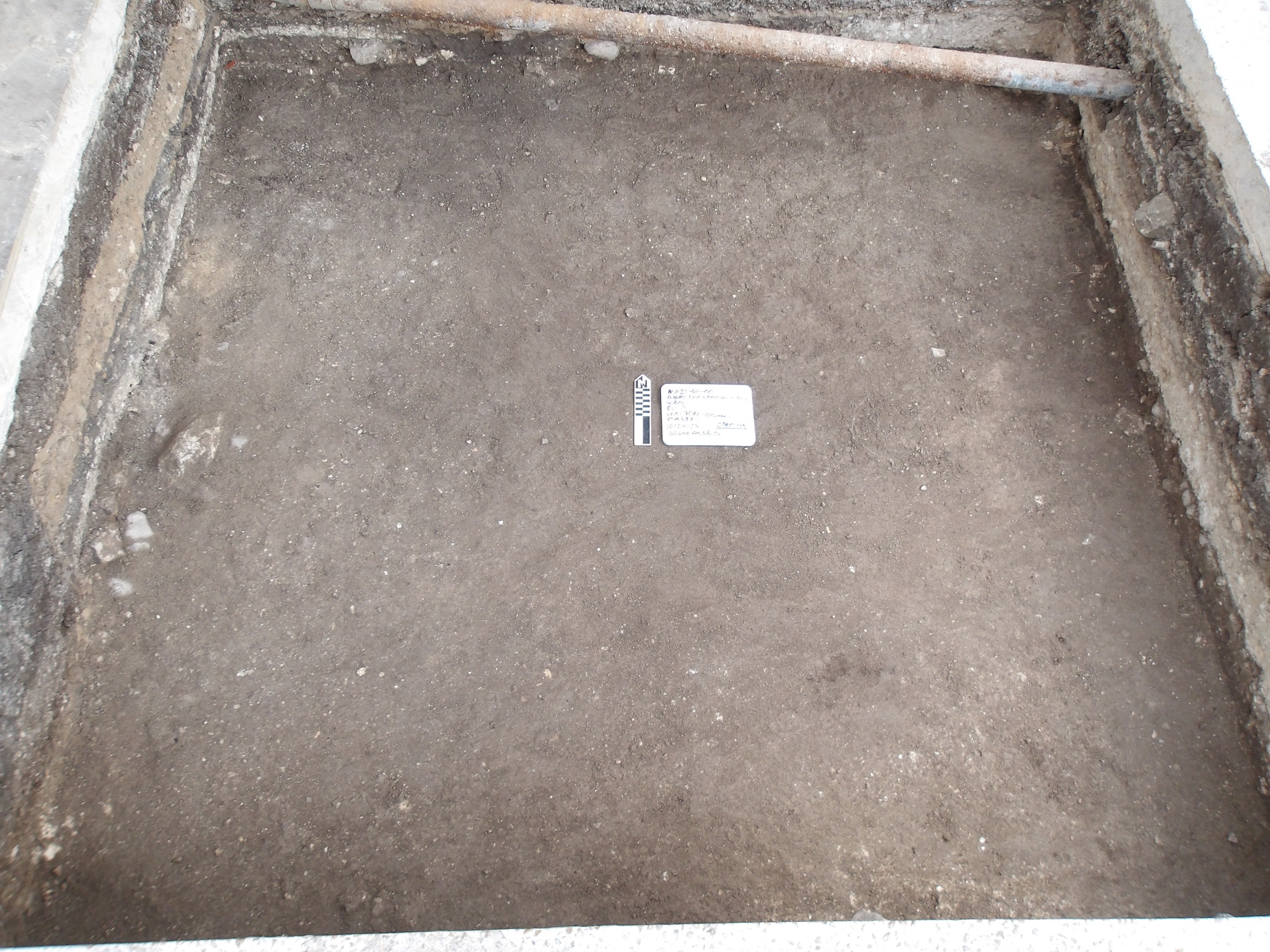Smooth bottom of an excavation unit with a marker and white board in the center