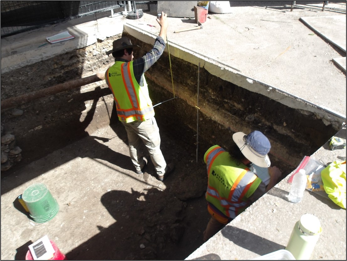 Two archaeologists looking at the east wall inside an excavation unit